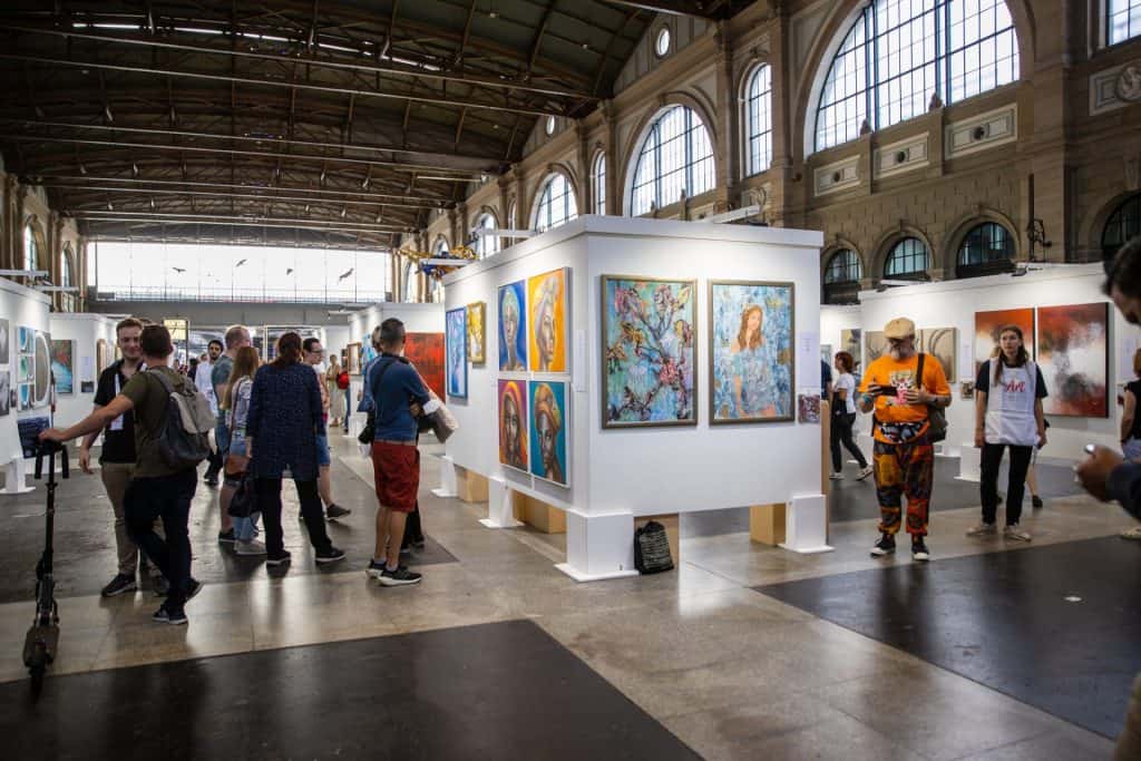 Posjetitelji se okupljaju oko modernih ekrana u galeriji u Zürichu, uživajući u raznolikim umjetničkim djelima prikazanim na izložbi ARTBOX.PROJECT