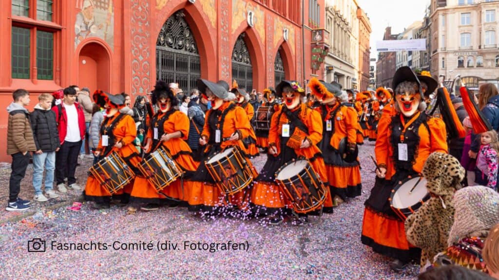 Maskirani sudionici u narančastim kostimima s bubnjevima na Basler Fasnachtu ispred gradske vijećnice.