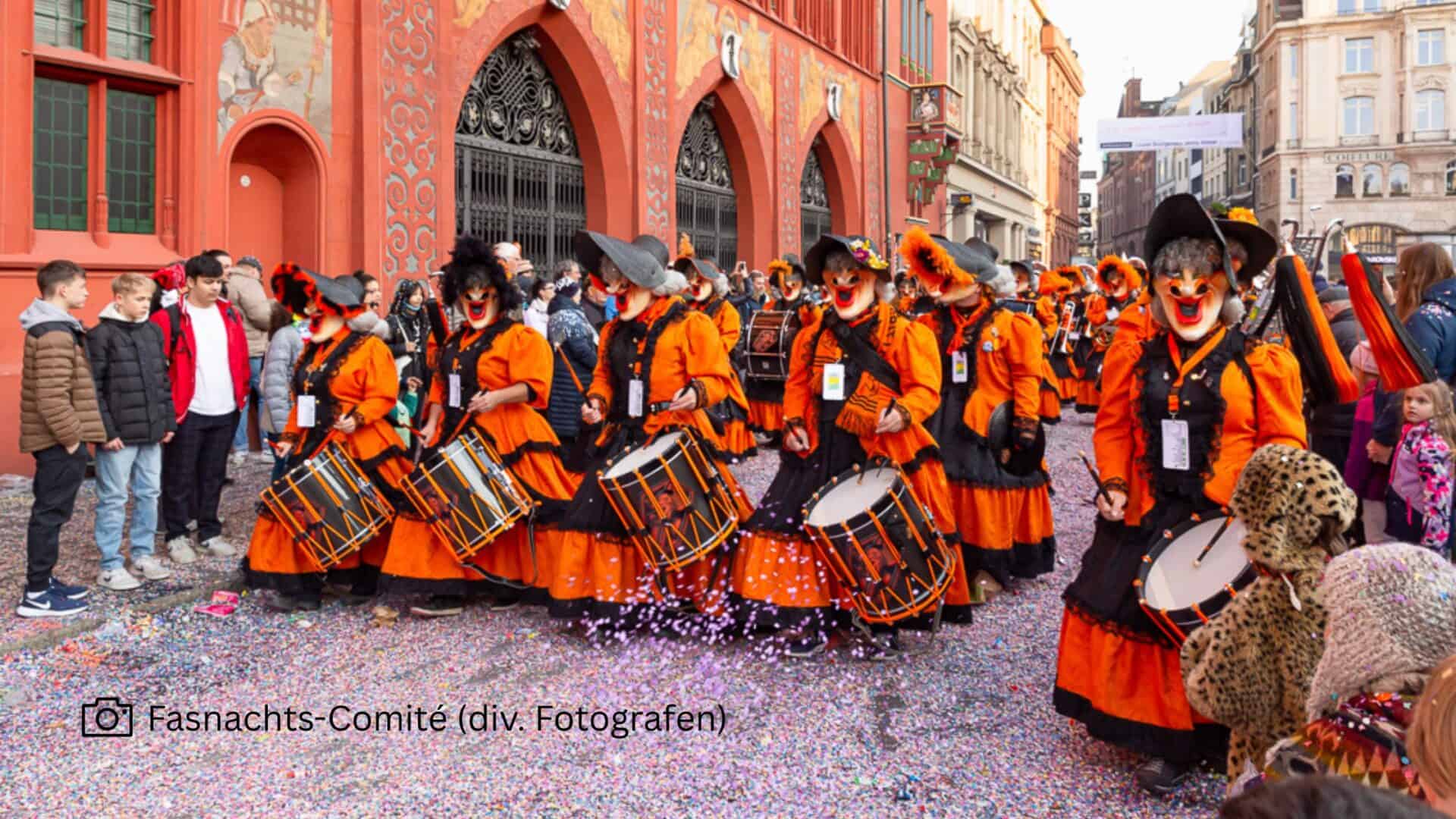 Maskirani sudionici u narančastim kostimima s bubnjevima na Basler Fasnachtu ispred gradske vijećnice.