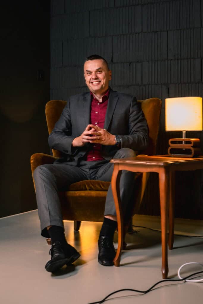 Komičar Saša Turković u sivom odijelu sjedi u žutom baršunastom naslonjaču, najavljujući stand-up u Badenu za Croatis.ch. Foto: Marko Lopac