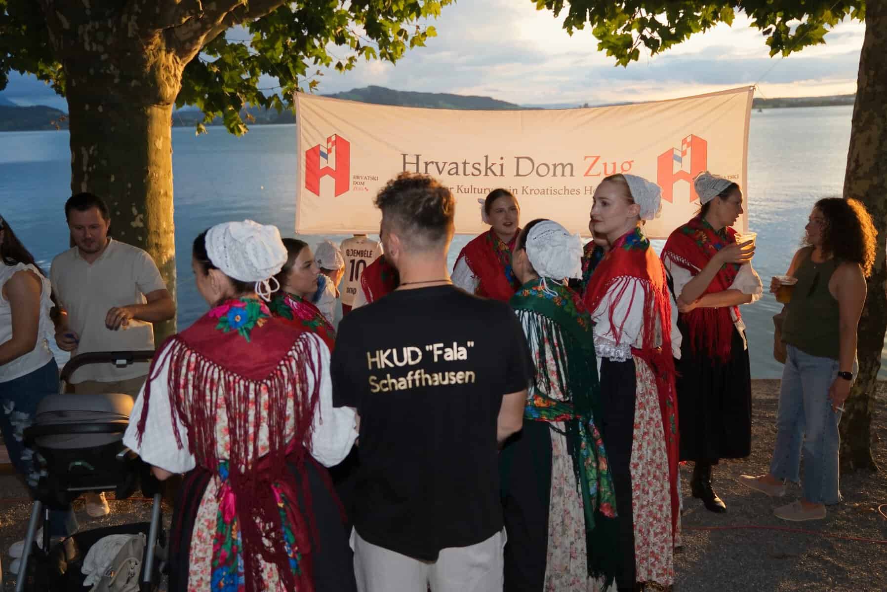 Članovi Hrvatskog doma Zug i plesačice HKUD-a Fala u narodnim nošnjama okupljeni ispred transparenta na obali jezera u Zugu